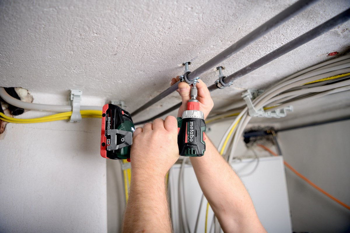 Un lavoratore usa un trapano a batteria per fissare dei tubi al soffitto.