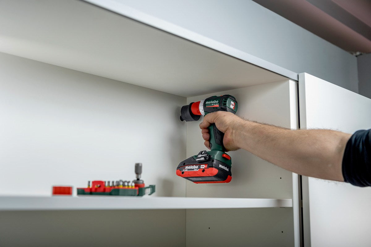 Una mano tiene un trapano a batteria verde e rosso all'interno di un mobile bianco.