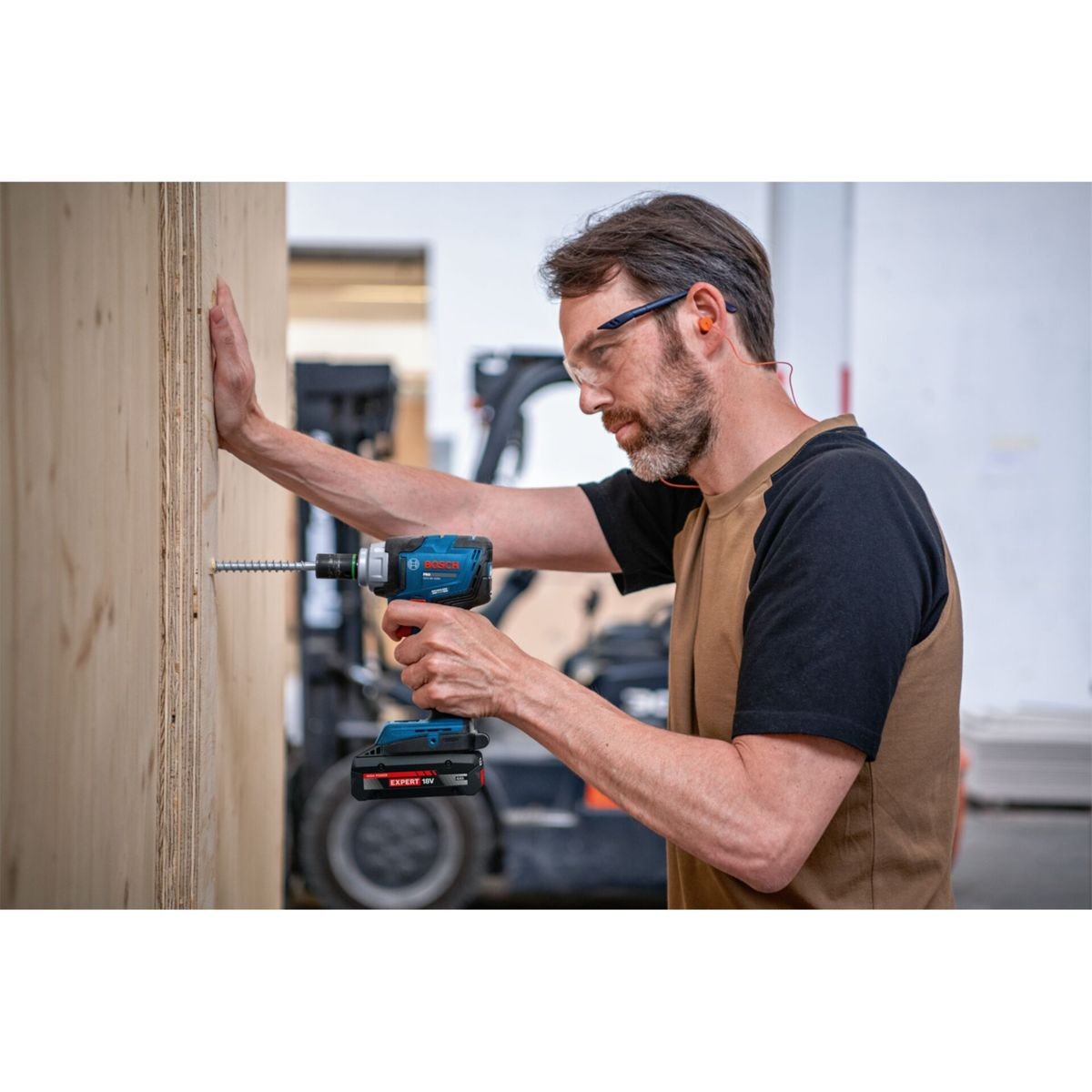 Un artigiano fora una tavola di legno con un trapano a batteria blu.