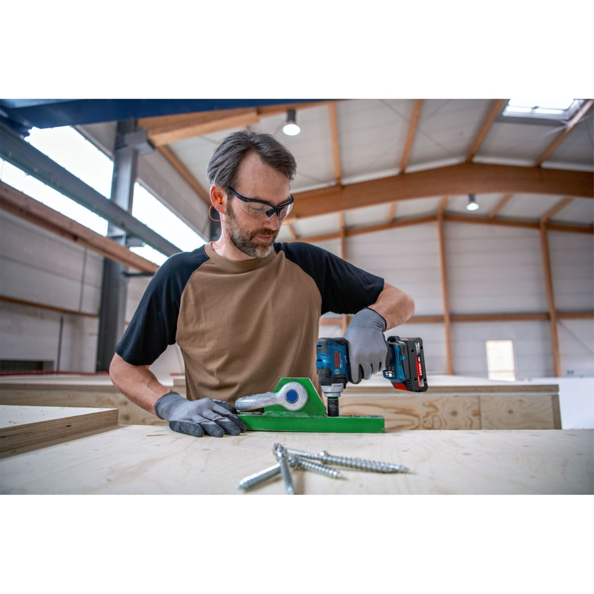 Un lavoratore con occhiali di protezione e guanti usa un utensile elettrico sul legno.