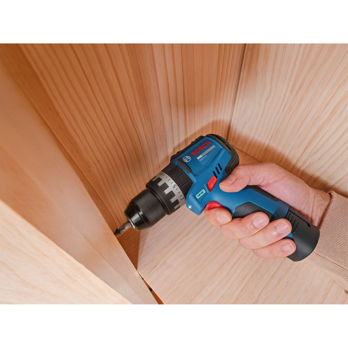 Una mano tiene un avvitatore a batteria Bosch blu mentre avvita nel legno.