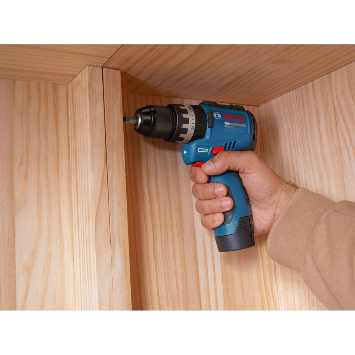 Una mano tiene un trapano a batteria Bosch blu contro una parete di legno.
