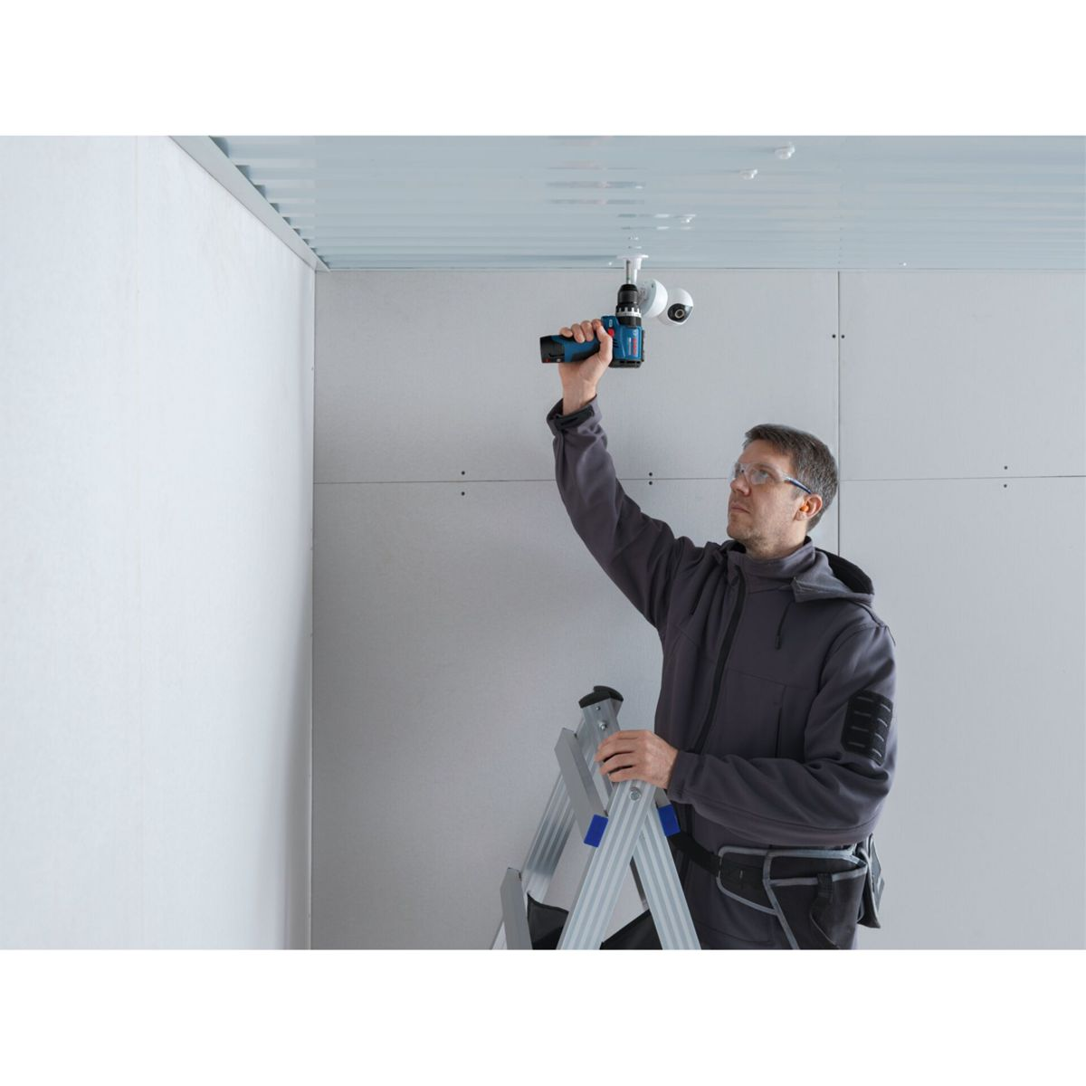 Un tecnico in piedi su una scala fora il soffitto.