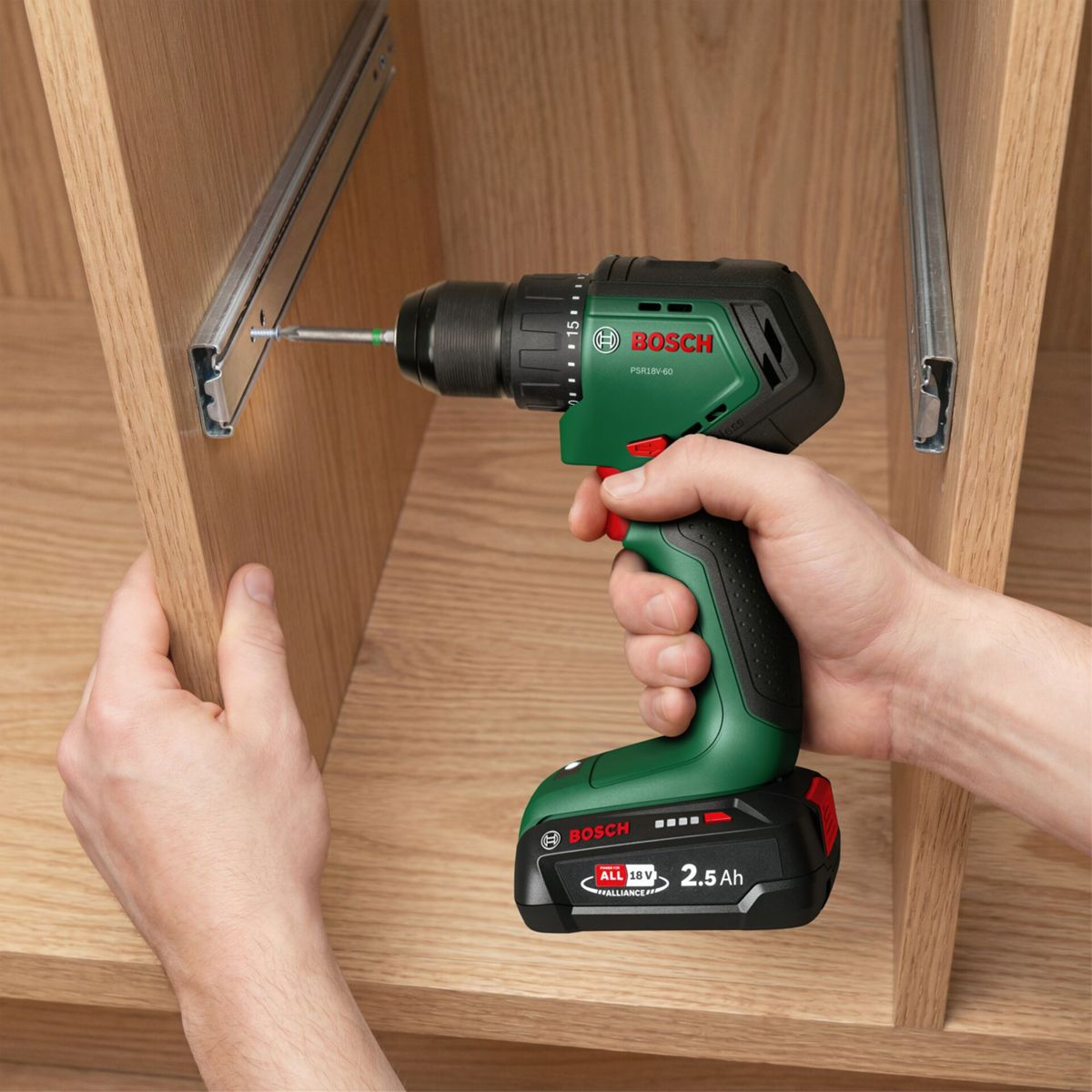 Una mano tiene un trapano a batteria Bosch verde e avvita una guida in un mobile in legno.
