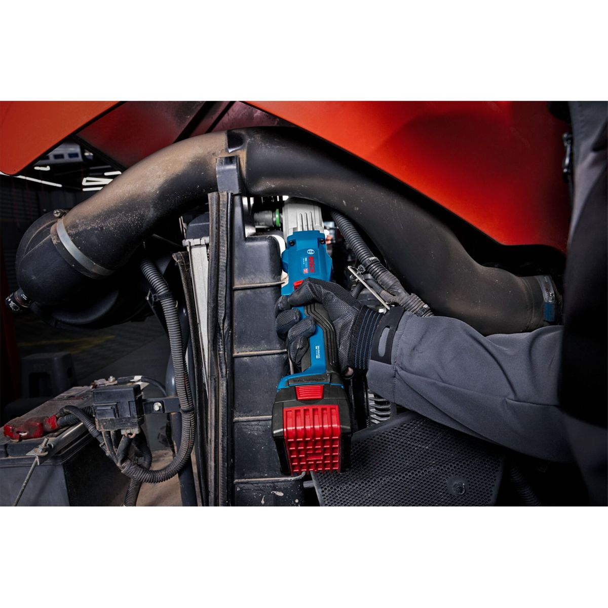 Una mano guantata tiene un elettroutensile blu e rosso all'interno di uno stretto vano motore.