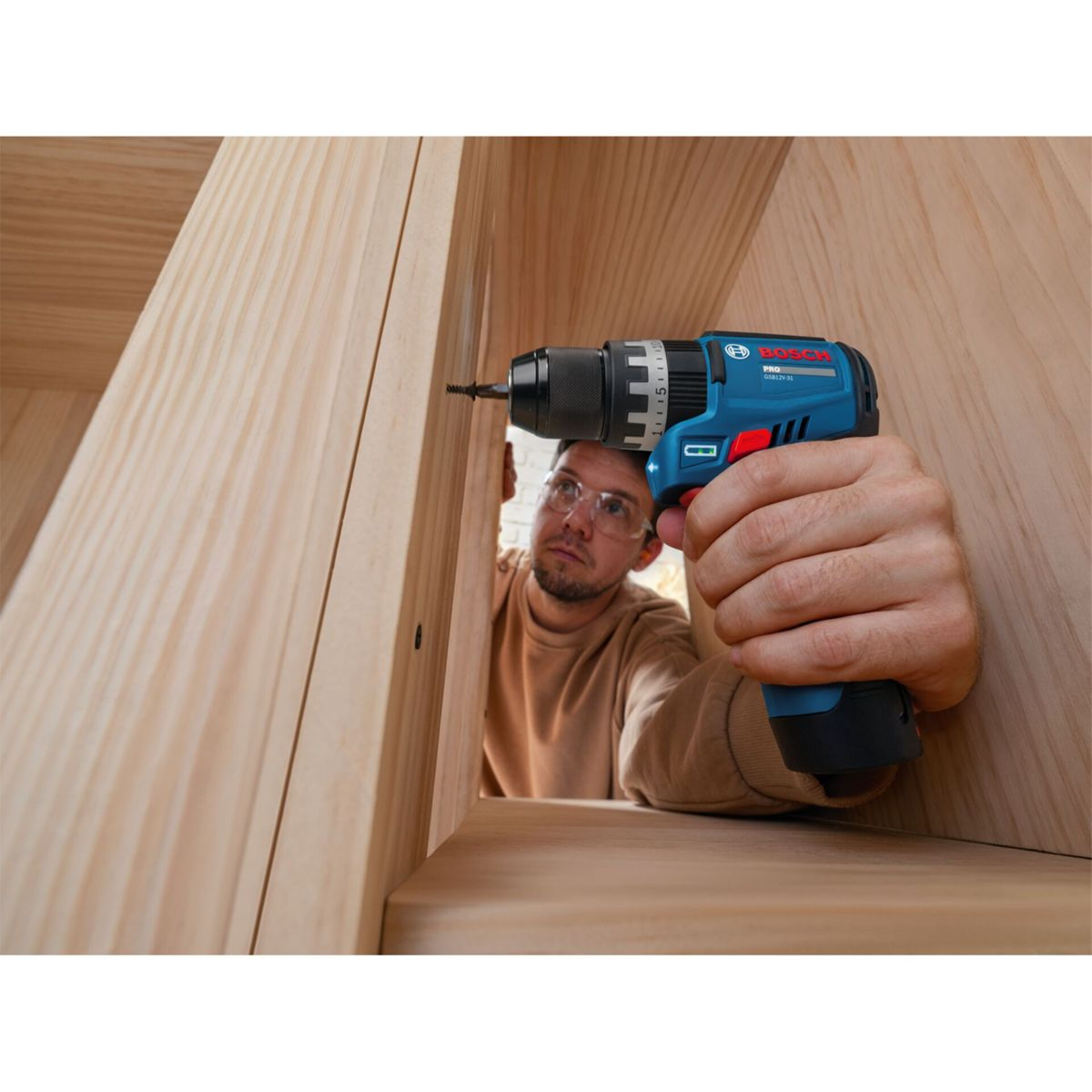 Un artigiano usa un avvitatore a batteria blu per fissare scaffali in legno.