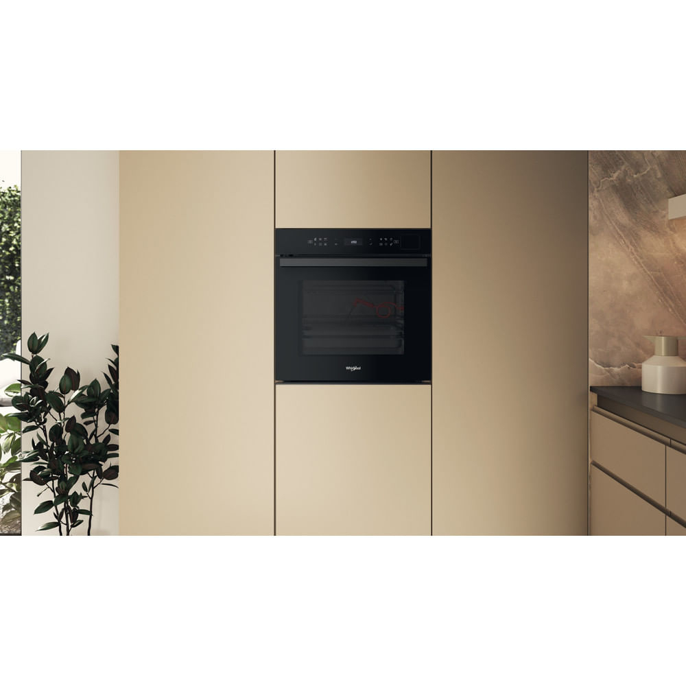 Un horno empotrable negro en muebles de cocina beige claro con una planta a la izquierda y una encimera a la derecha.