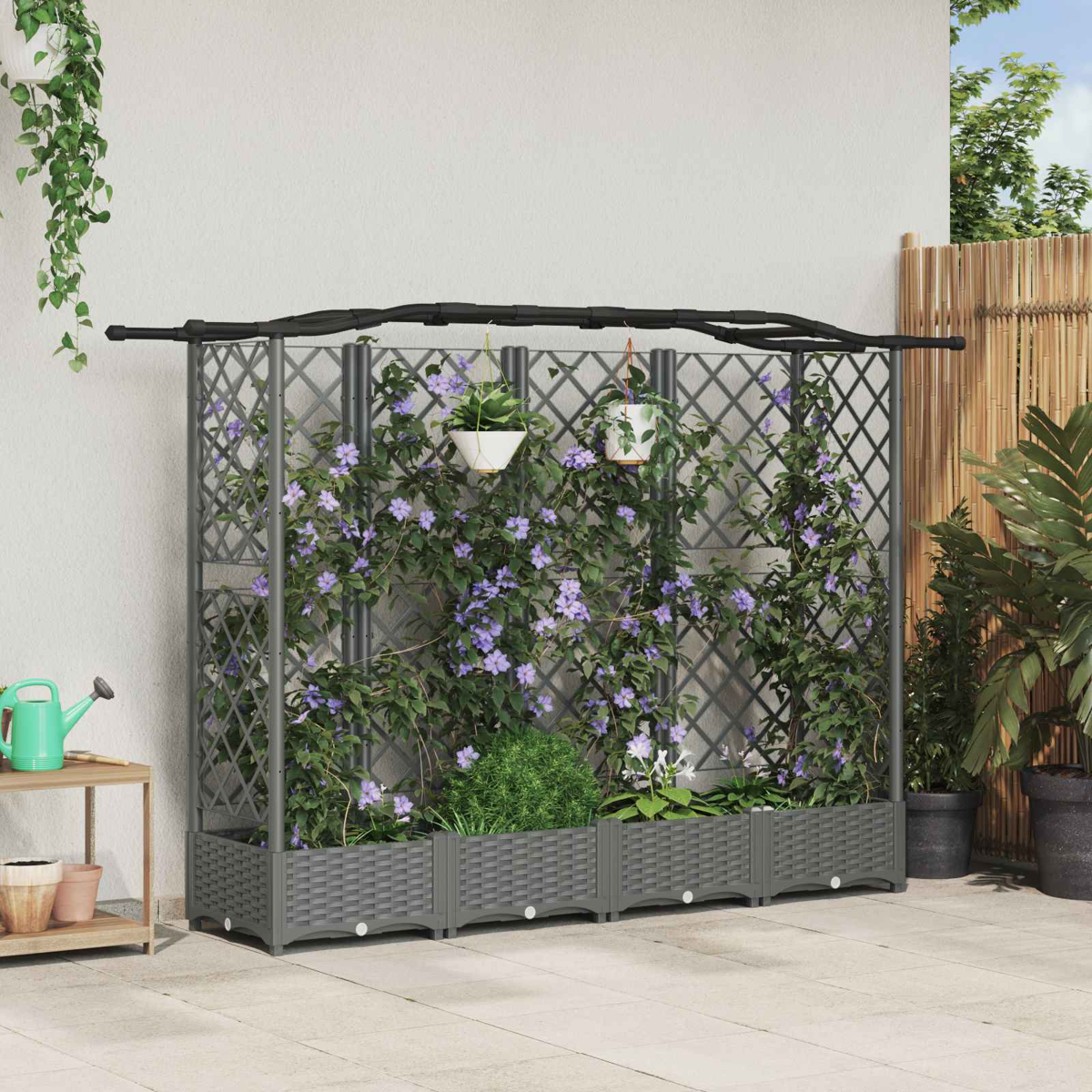 Ein graues Spalier mit kletternden lila Blüten steht auf einer Terrasse, mit Töpfen und Pflanzen.