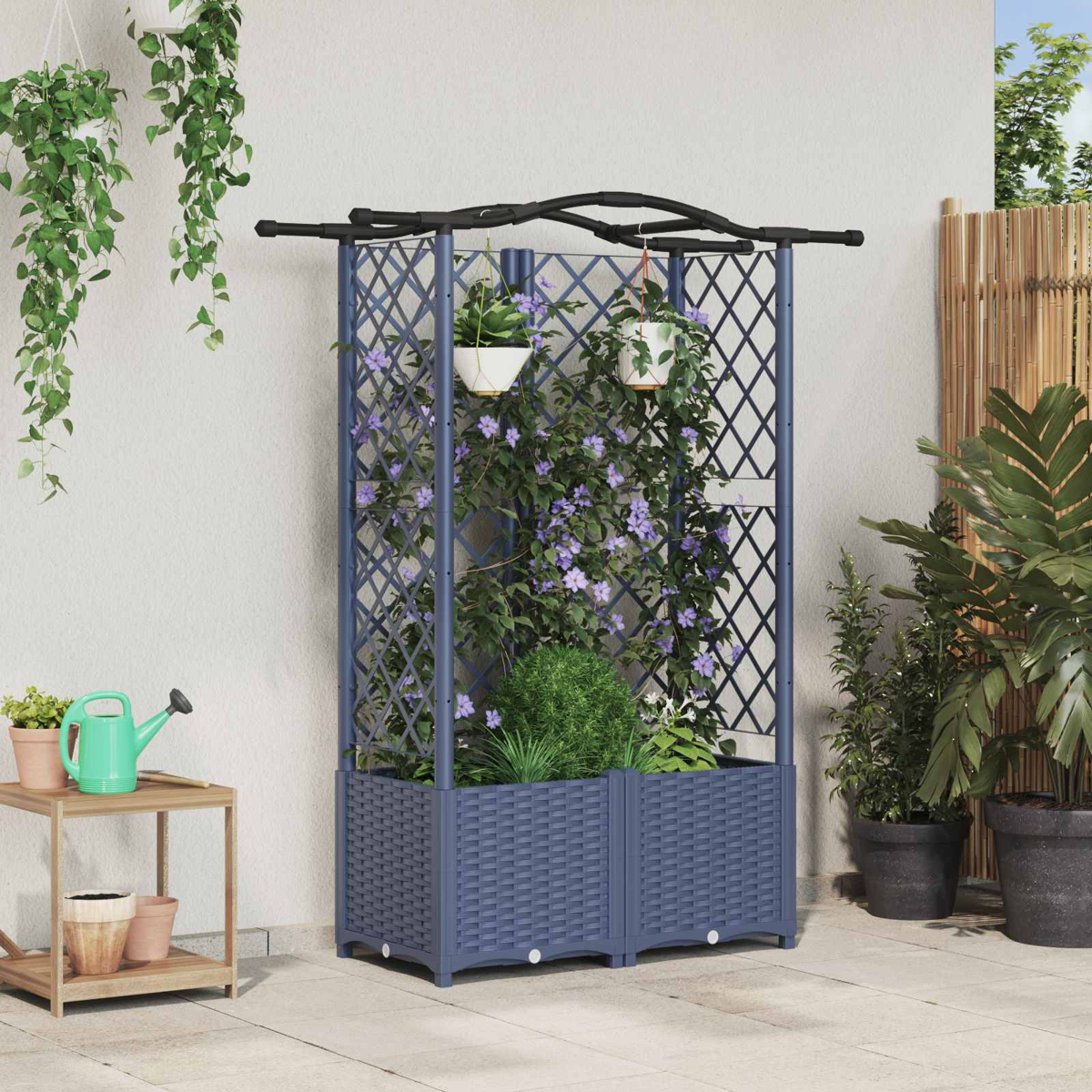 Ein blaues Rankgitter mit Hochbeet, bepflanzt mit violetten Blumen, steht auf einer Terrasse neben Pflanzen und einer Gießkanne.