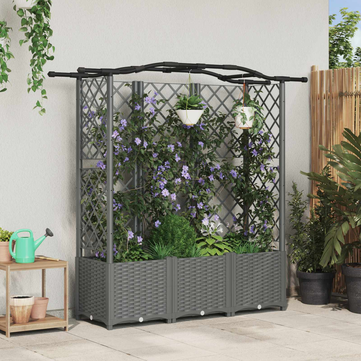 Graues Gartenspalier mit Pflanzkasten, kletternden lila Blumen, Hängetöpfen und kleinem Beistelltisch auf der Terrasse.