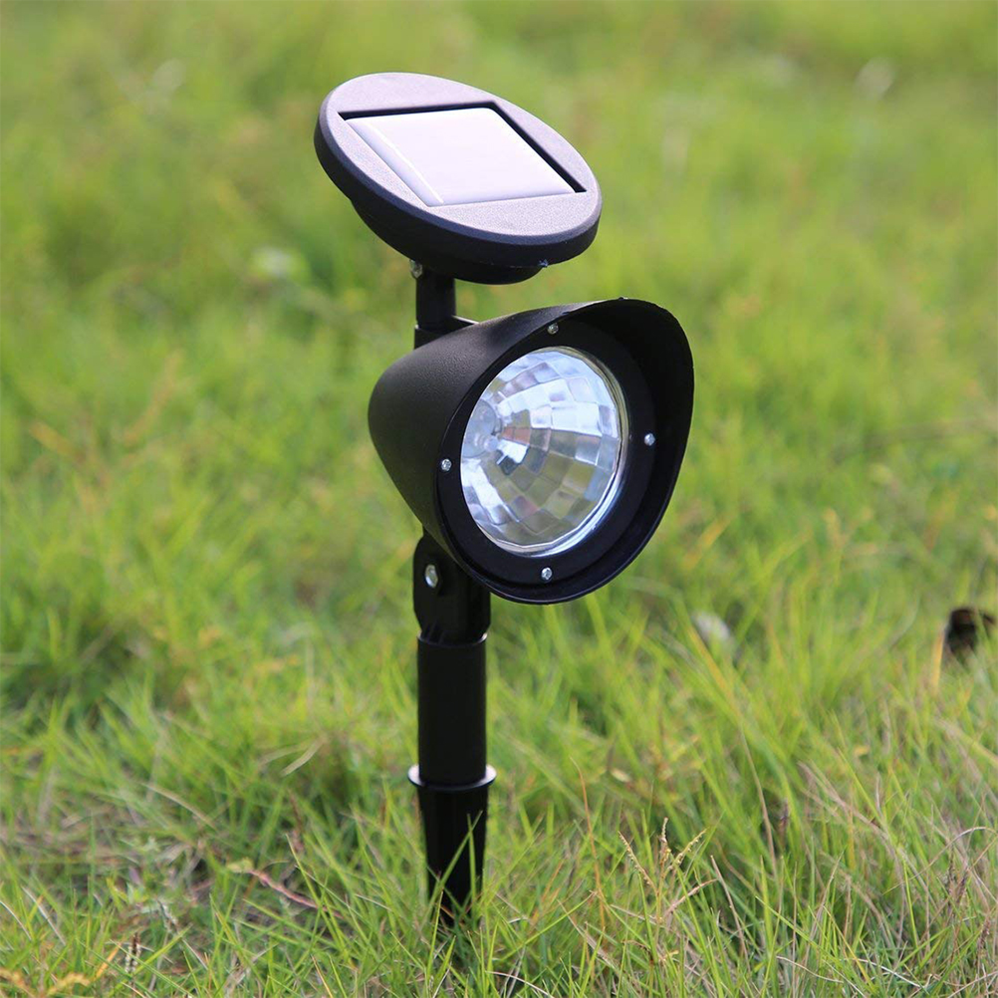 Eine schwarze Solarlampe steckt in einer grünen Wiese.