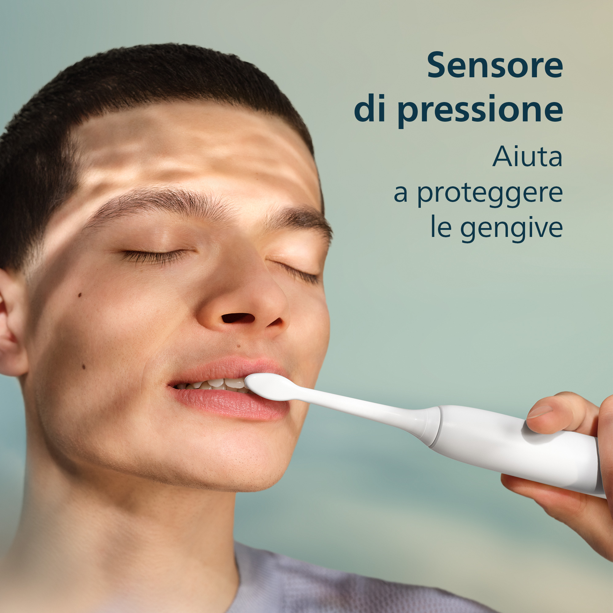 Un giovane si lava i denti con uno spazzolino elettrico bianco. Testo a destra.