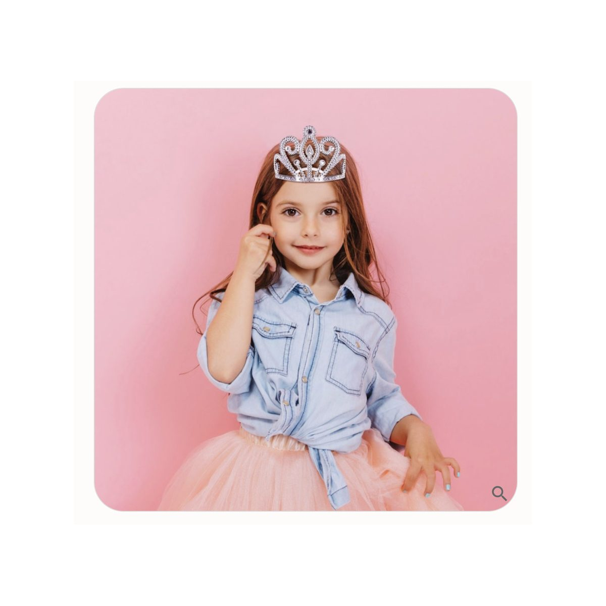 Ein kleines Mädchen mit einer silbernen Tiara, einem Jeanshemd und einem rosa Tüllrock vor rosa Hintergrund.