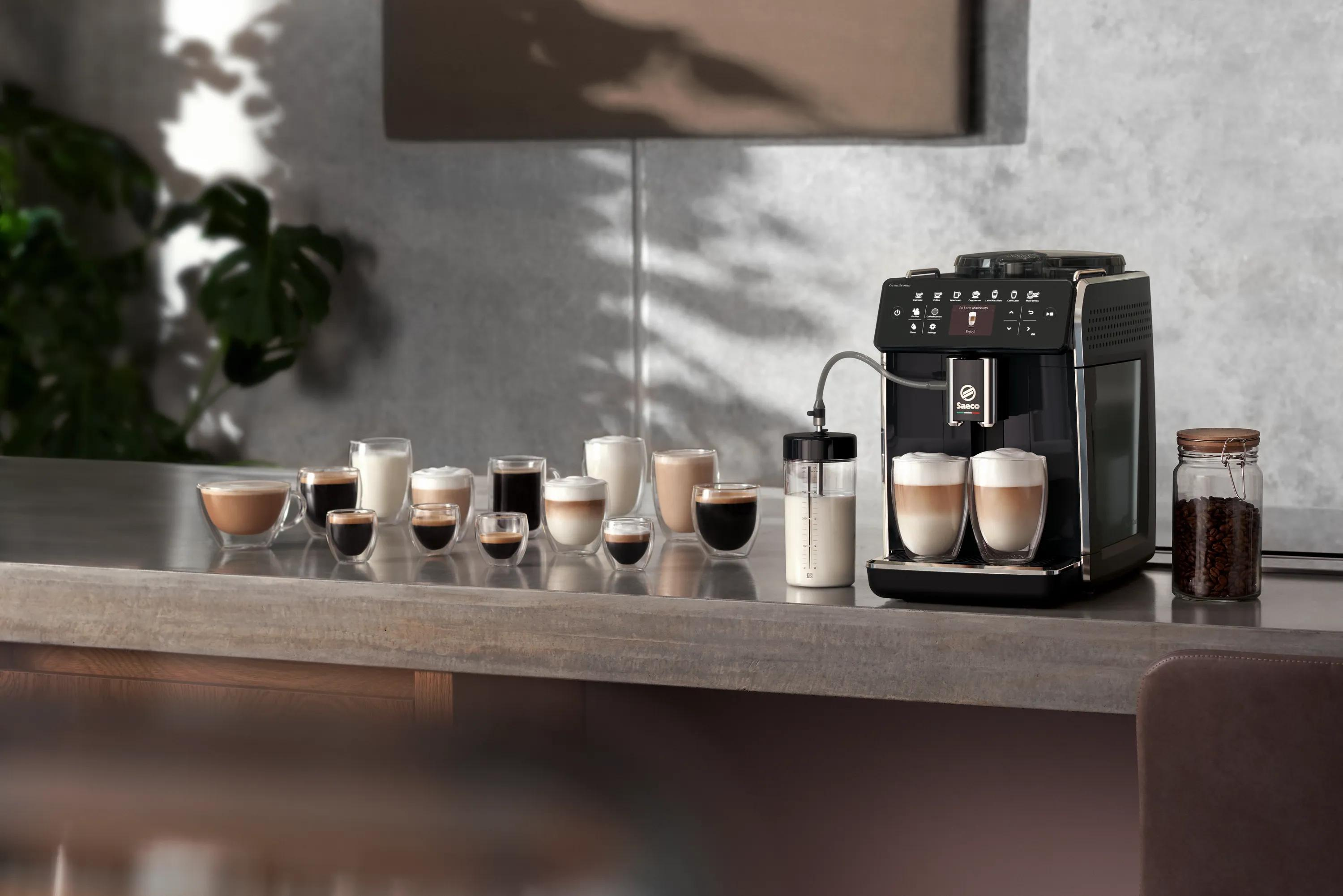 Macchina da caffè nera su piano di lavoro con varie specialità di caffè in bicchieri e barattolo di chicchi.
