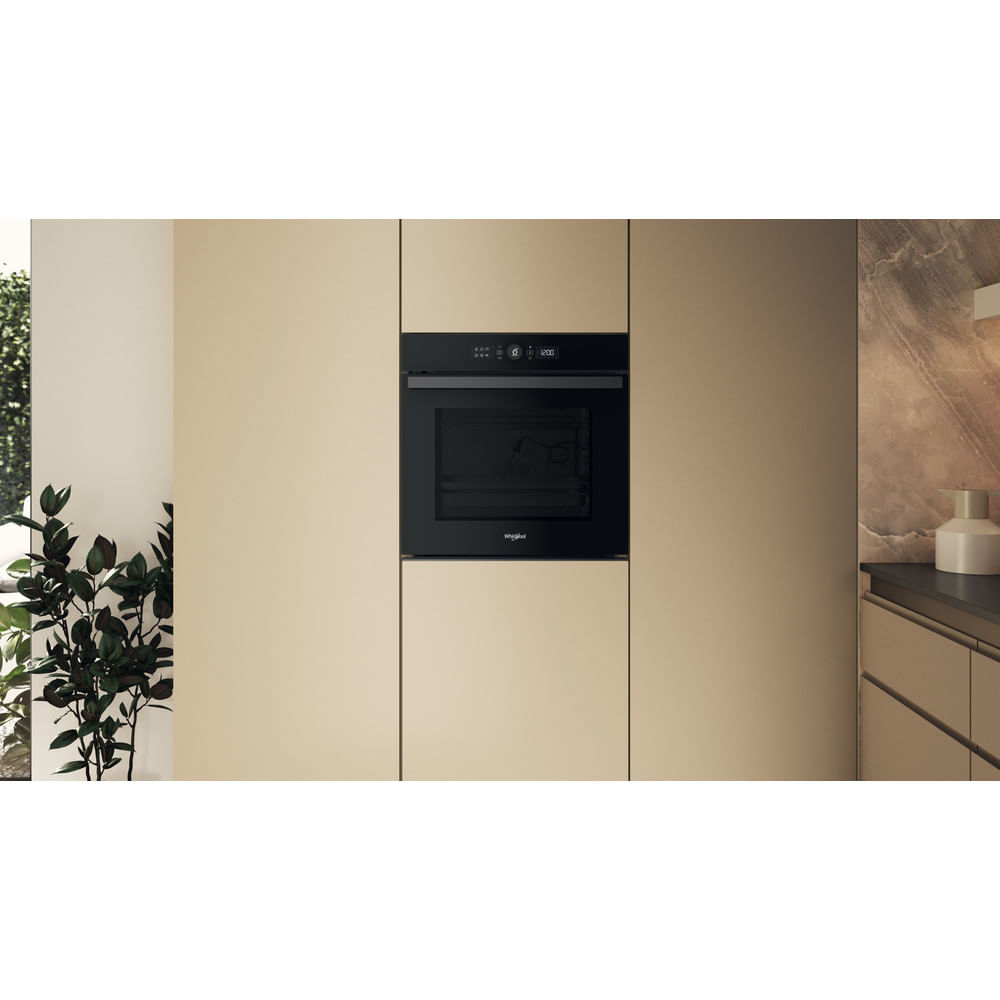 Un horno empotrable negro en muebles de cocina beige, con una planta a la izquierda y encimera a la derecha.
