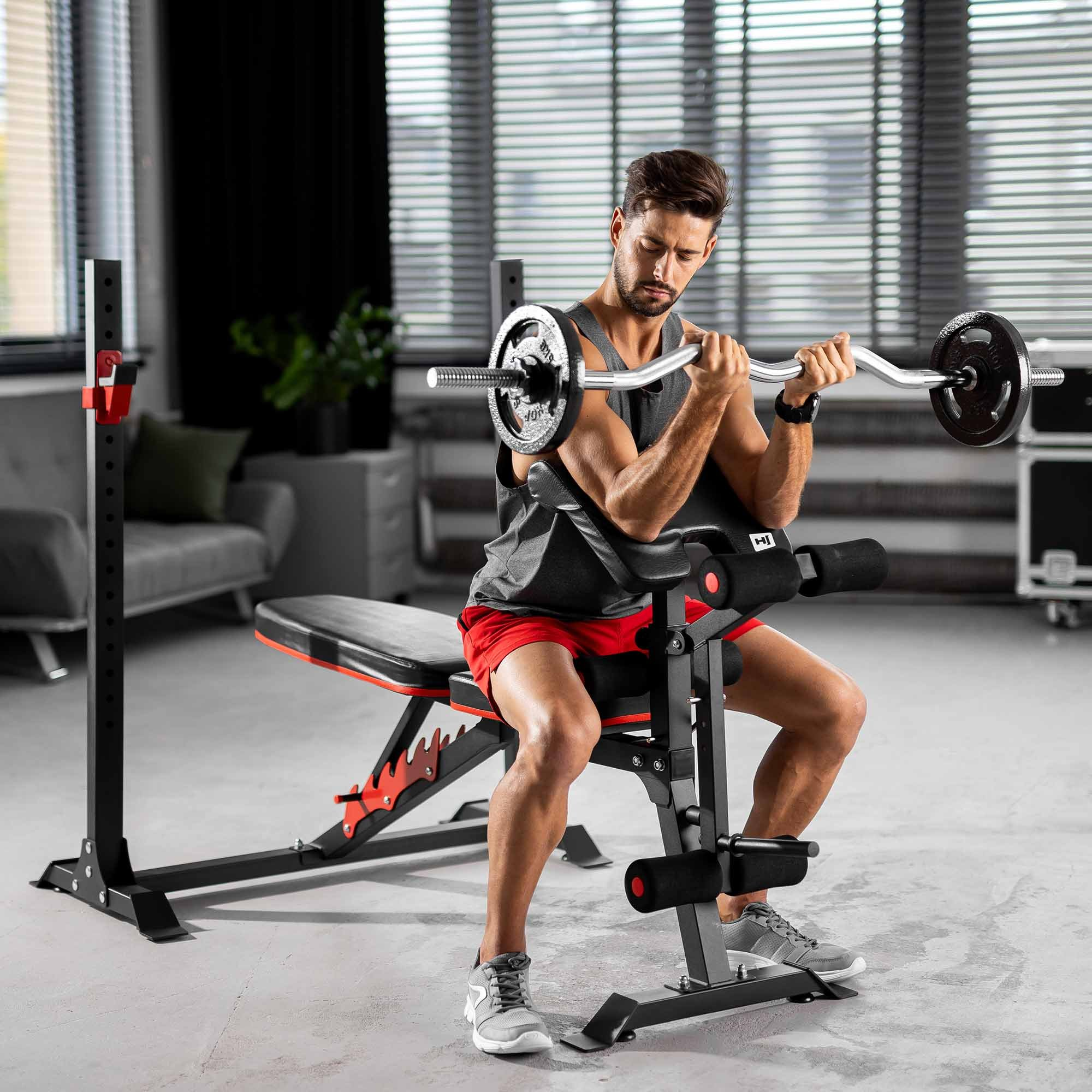 Ein Mann sitzt auf einer Trainingsbank und hebt eine SZ-Stange mit Gewichten in einem modernen Raum.