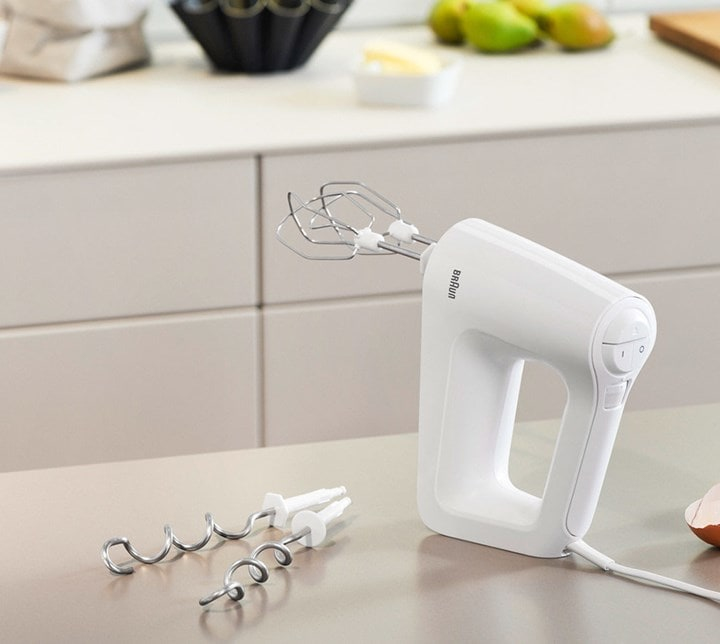 Un frullatore a mano bianco con due fruste e due ganci per impasto su un piano cucina.