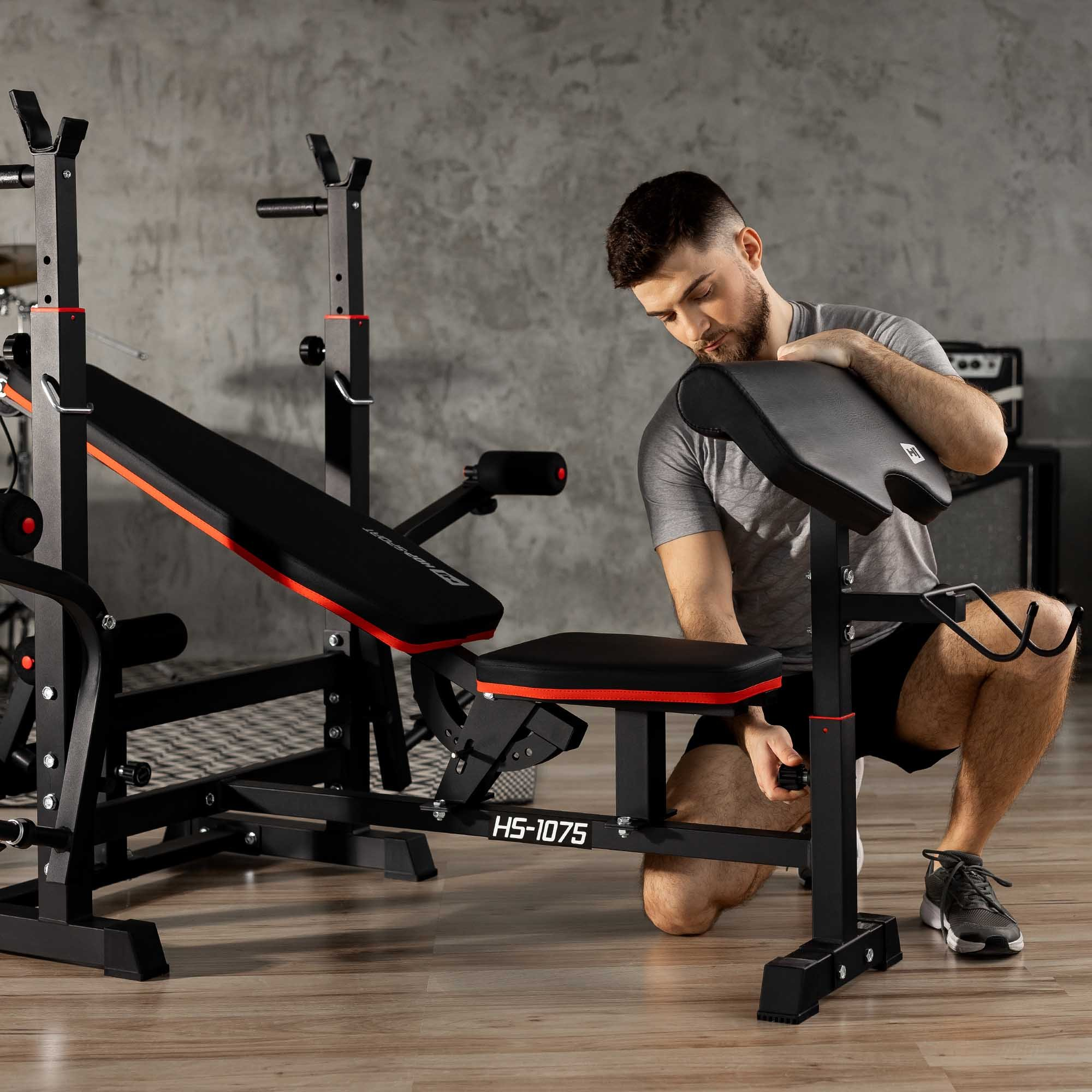 Ein Mann passt die Höhe einer Hantelbank mit rotem Rand im Fitnessstudio an.