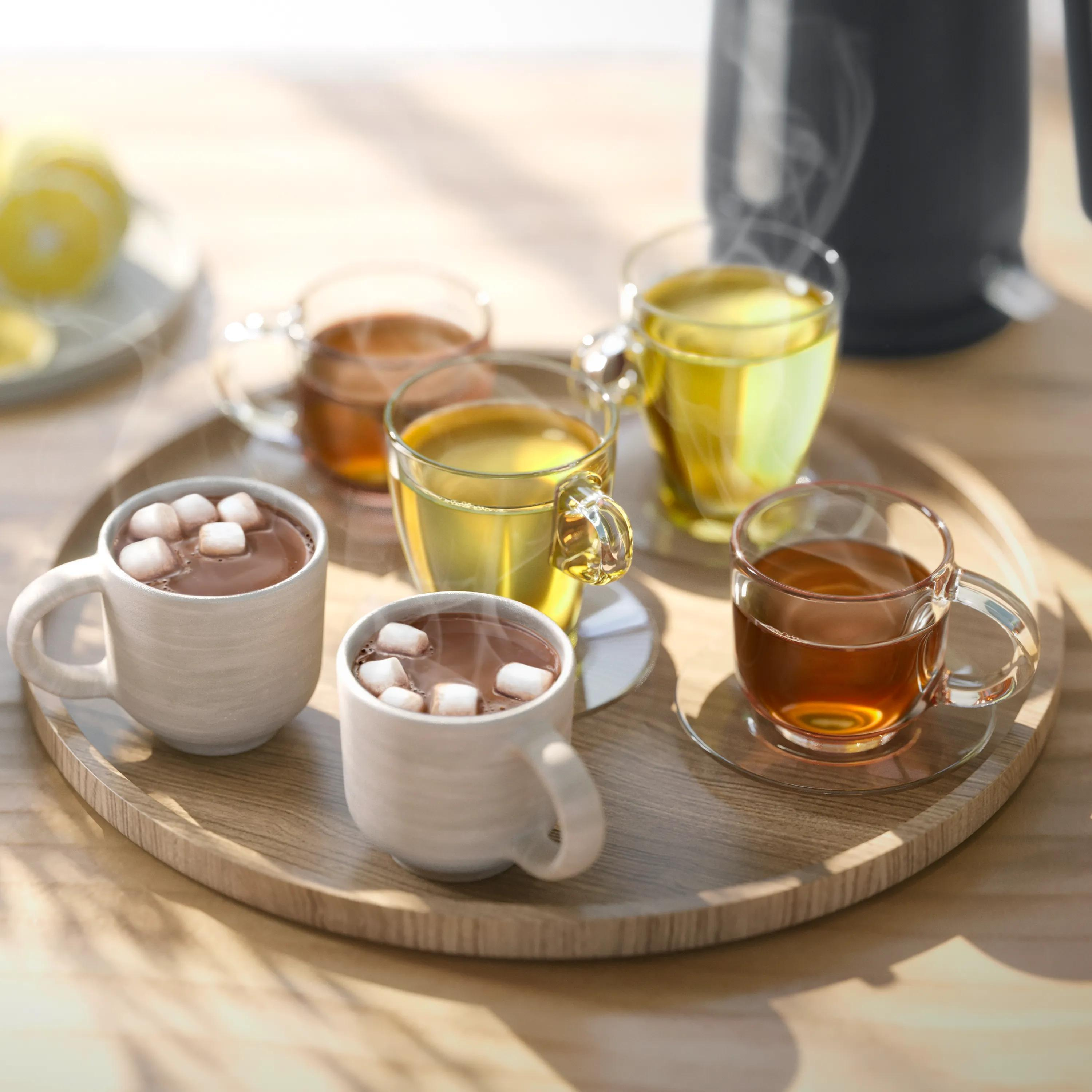 Un vassoio di legno contiene tazze di cioccolata calda con marshmallow e tè fumante.