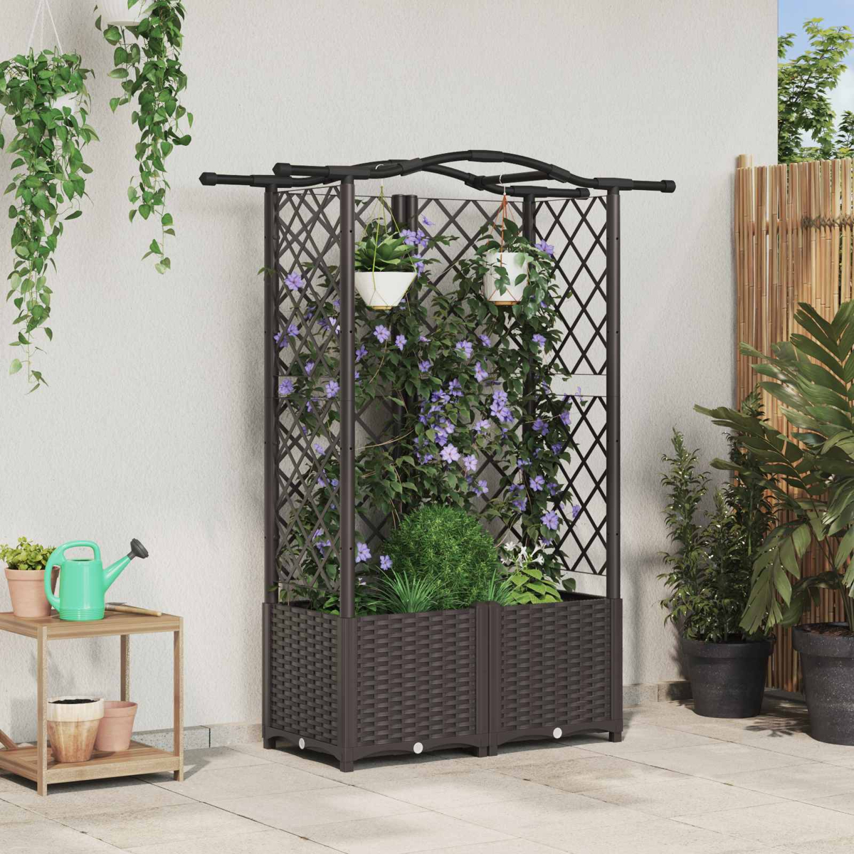 Ein schwarzes Pflanzgefäß mit Spalier und violetten Kletterpflanzen steht vor einer hellen Wand auf einer Terrasse.