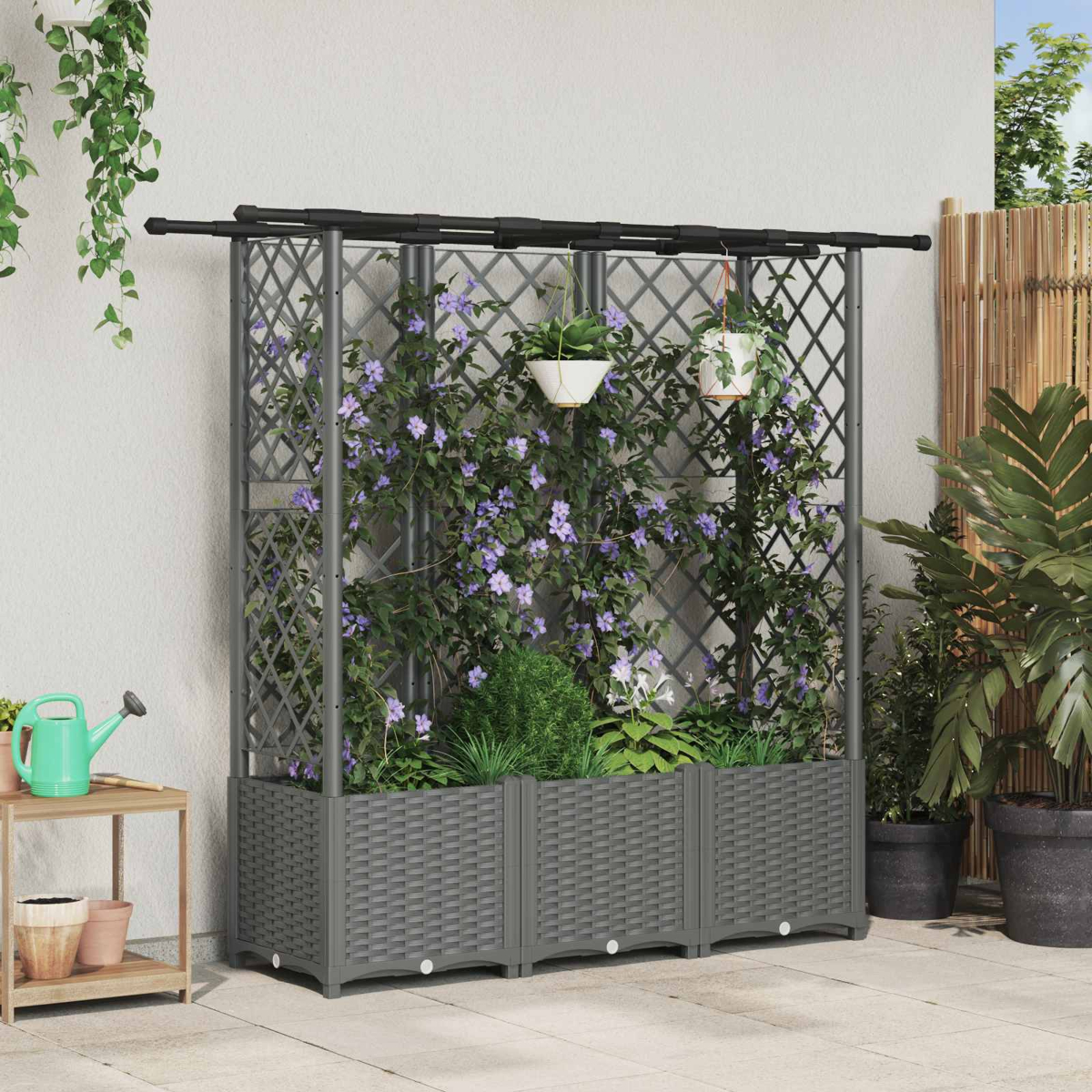 Graues Garten-Spalier mit Pflanzkübeln, violetten Blüten und hängenden Töpfen vor heller Wand.