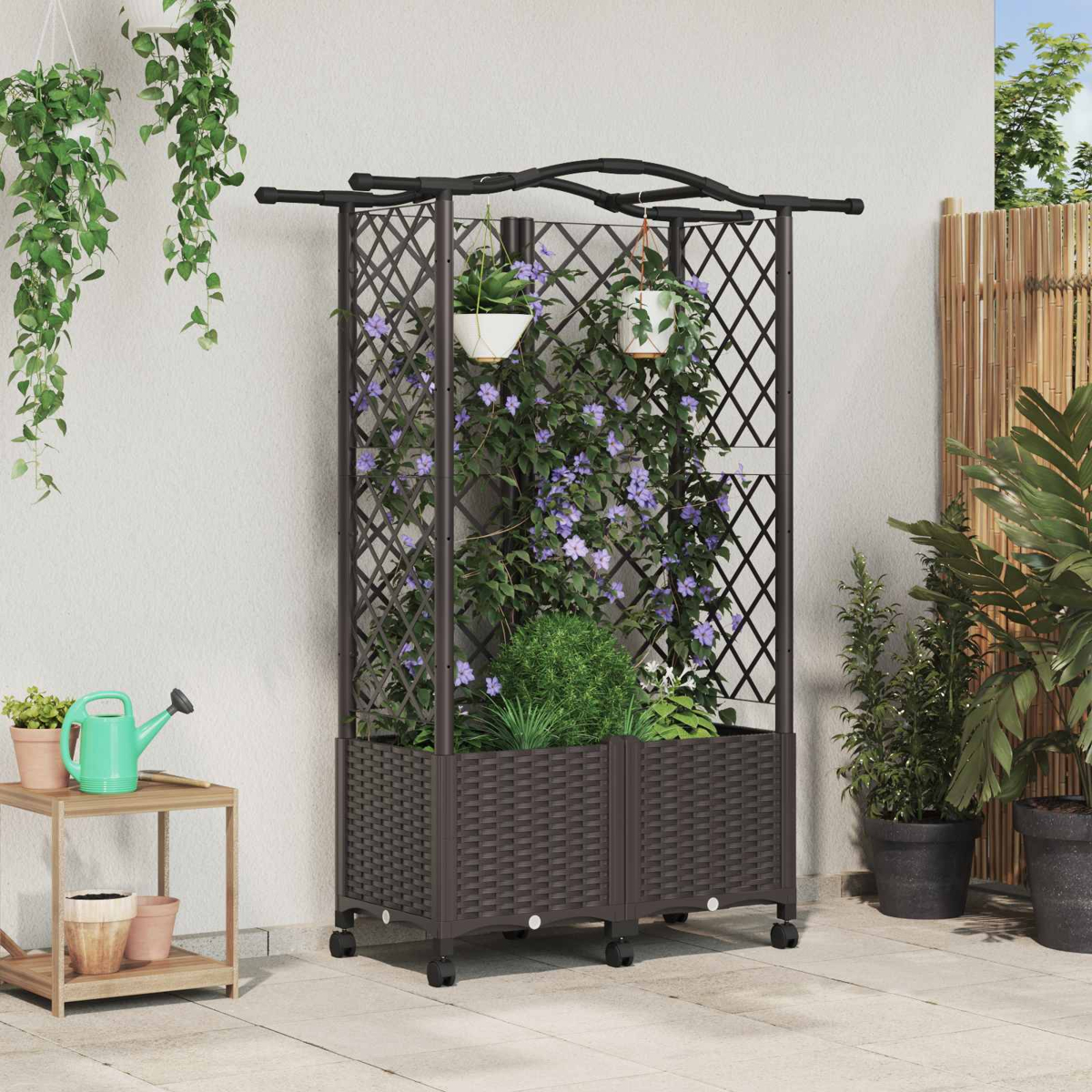 Brauner Pflanzkübel mit Spalier und Kletterpflanzen, stehend auf einer Terrasse mit Blumen und Gießkanne.