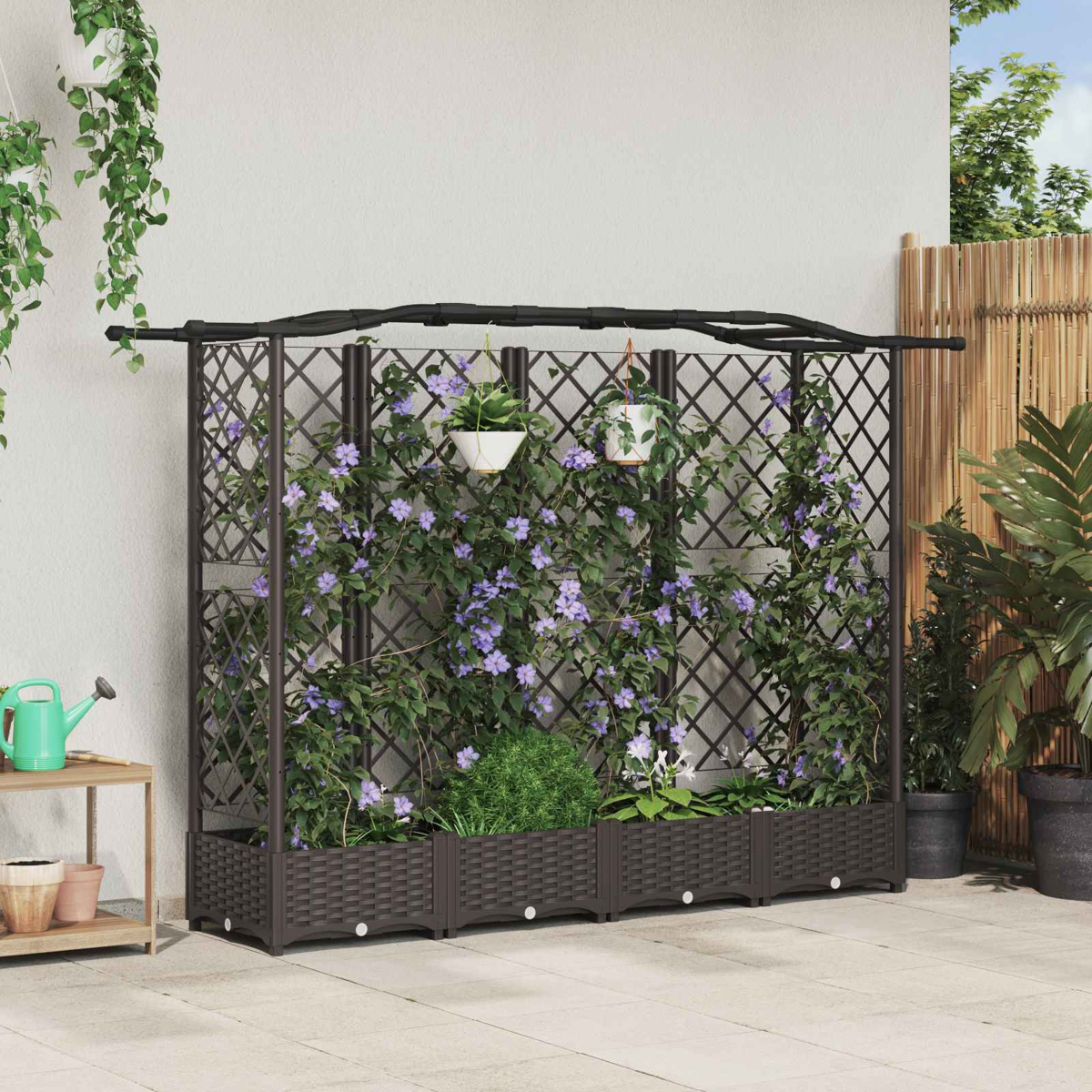 Ein schwarzes Spalier mit braunen Pflanzkästen, bewachsen mit Kletterpflanzen und violetten Blüten, steht an einer Wand.