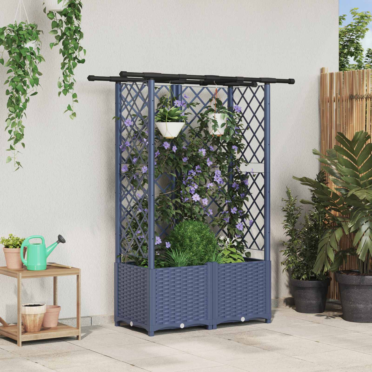 Ein blauer Kunststoff-Pflanzkasten mit Rankgitter und violetten Kletterblumen auf einer Terrasse voller Topfpflanzen.