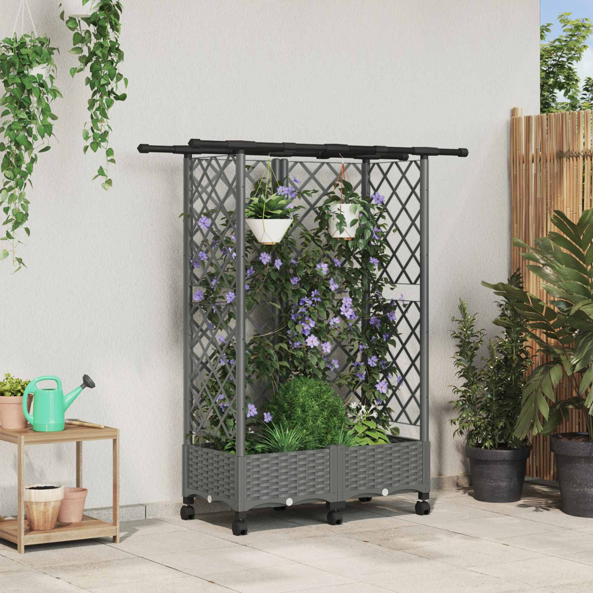 Graues Pflanzgefäß mit Spalier und violetten Kletterpflanzen auf Rollen, im Hintergrund weiße Wand.