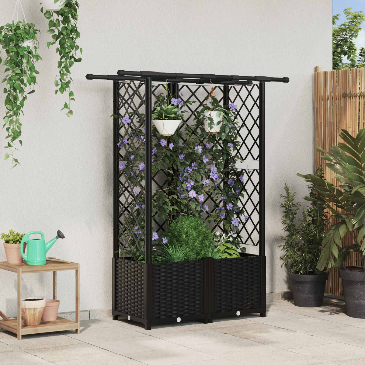 Schwarzes Rankgitter mit Pflanzkübeln, Kletterpflanzen und hängenden Blumen vor einer grauen Wand auf einer Terrasse.