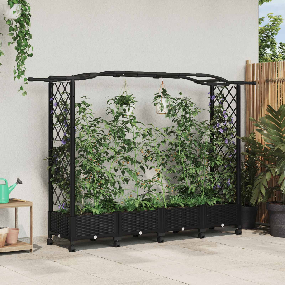 Ein schwarzes Hochbeet mit Rankgitter und Hängepflanzen steht auf einer Terrasse vor einer weißen Wand.