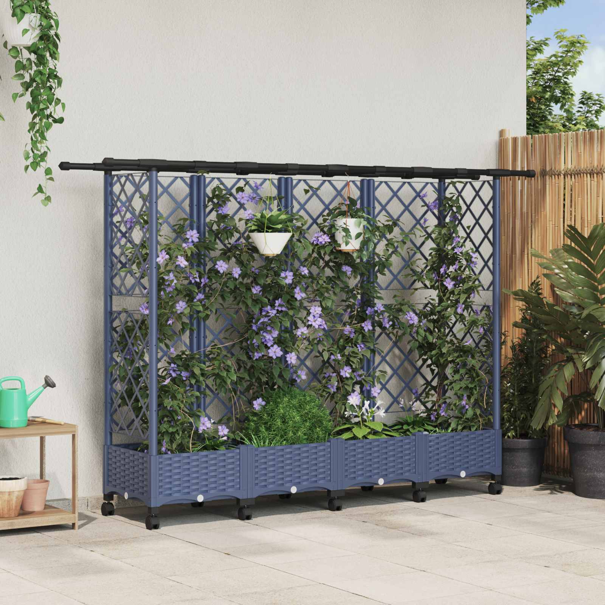 Ein blauer Rankkasten mit Rollen, bewachsen mit violetten Blumen und hängenden Töpfen vor einer Wand.
