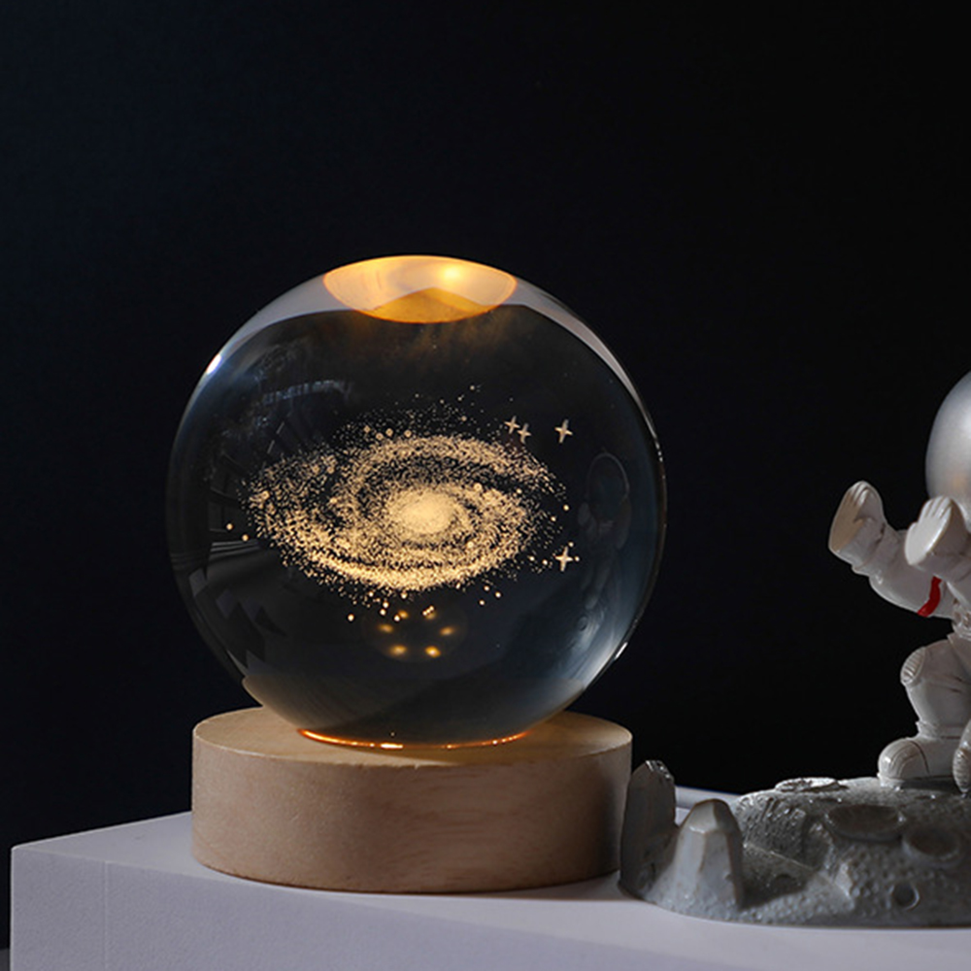Eine leuchtende Kristallkugel mit einer Galaxie auf einem Holzsockel neben einer Astronautenfigur.
