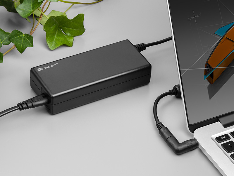 Un bloc d'alimentation noir connecté à un ordinateur portable et un câble sur un bureau gris.