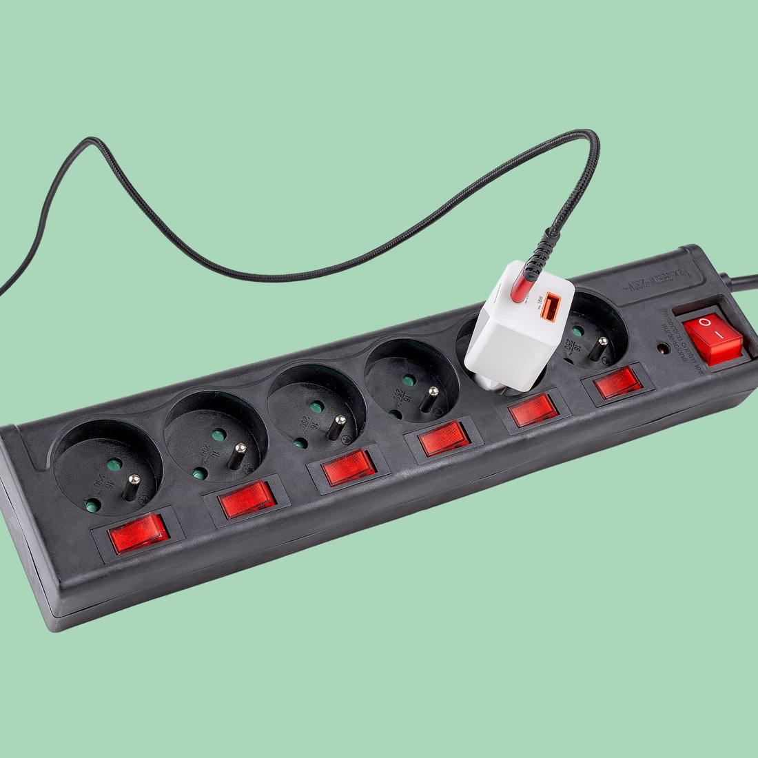 Schwarze Steckdosenleiste mit roten Schaltern und einem weißen USB-Ladegerät auf grünem Hintergrund.