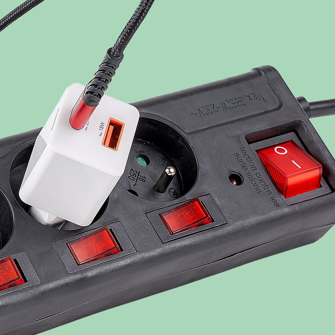 Schwarze Steckdosenleiste mit roten Schaltern und einem weißen USB-Ladegerät, das in einer Steckdose steckt.