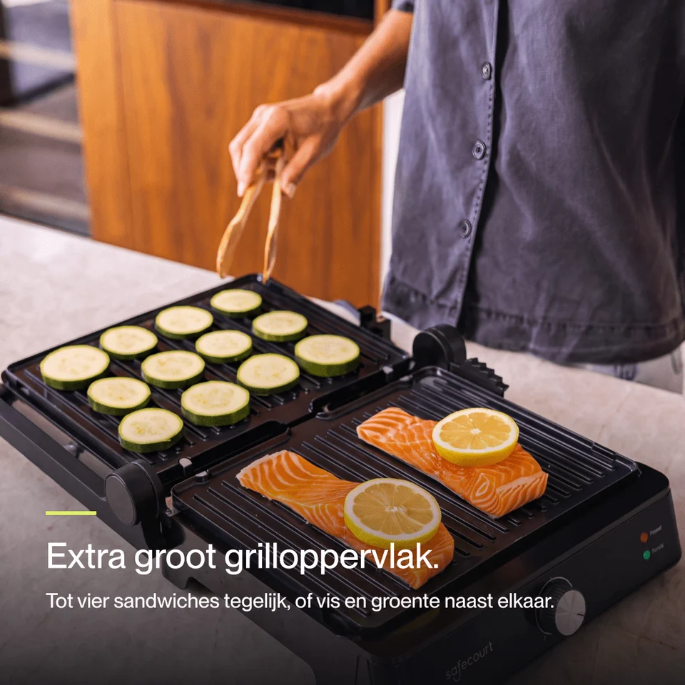 A person grilling zucchini slices on one side and salmon with lemon on the other on an electric grill.