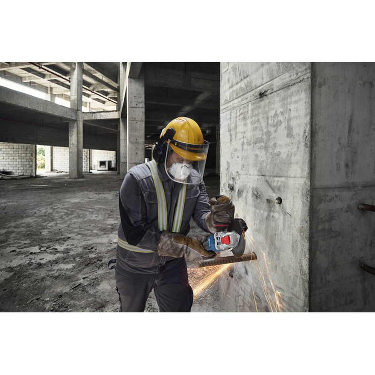 Ein Arbeiter in Schutzkleidung trennt Metall mit einer Flex und erzeugt Funken in einem Rohbau.