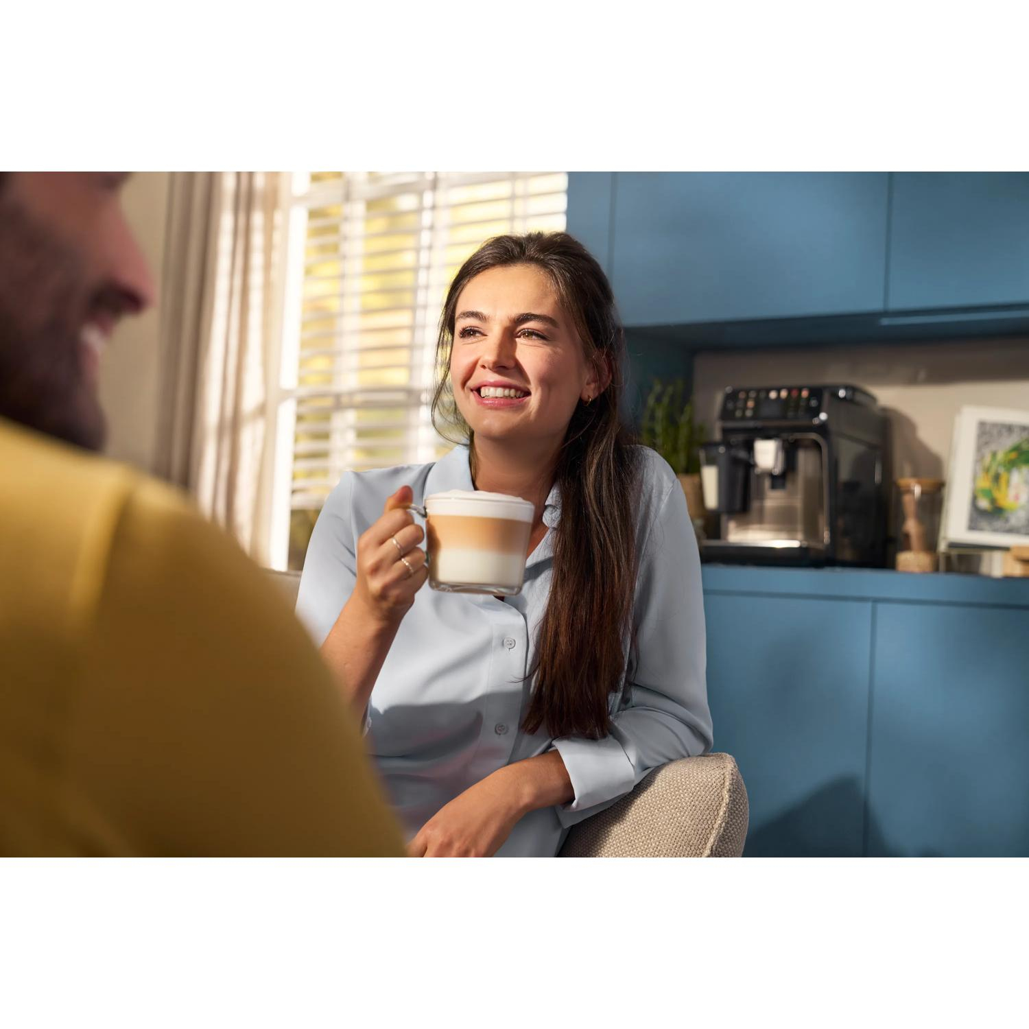 Uśmiechnięta kobieta z latte macchiato rozmawia z mężczyzną w kuchni.