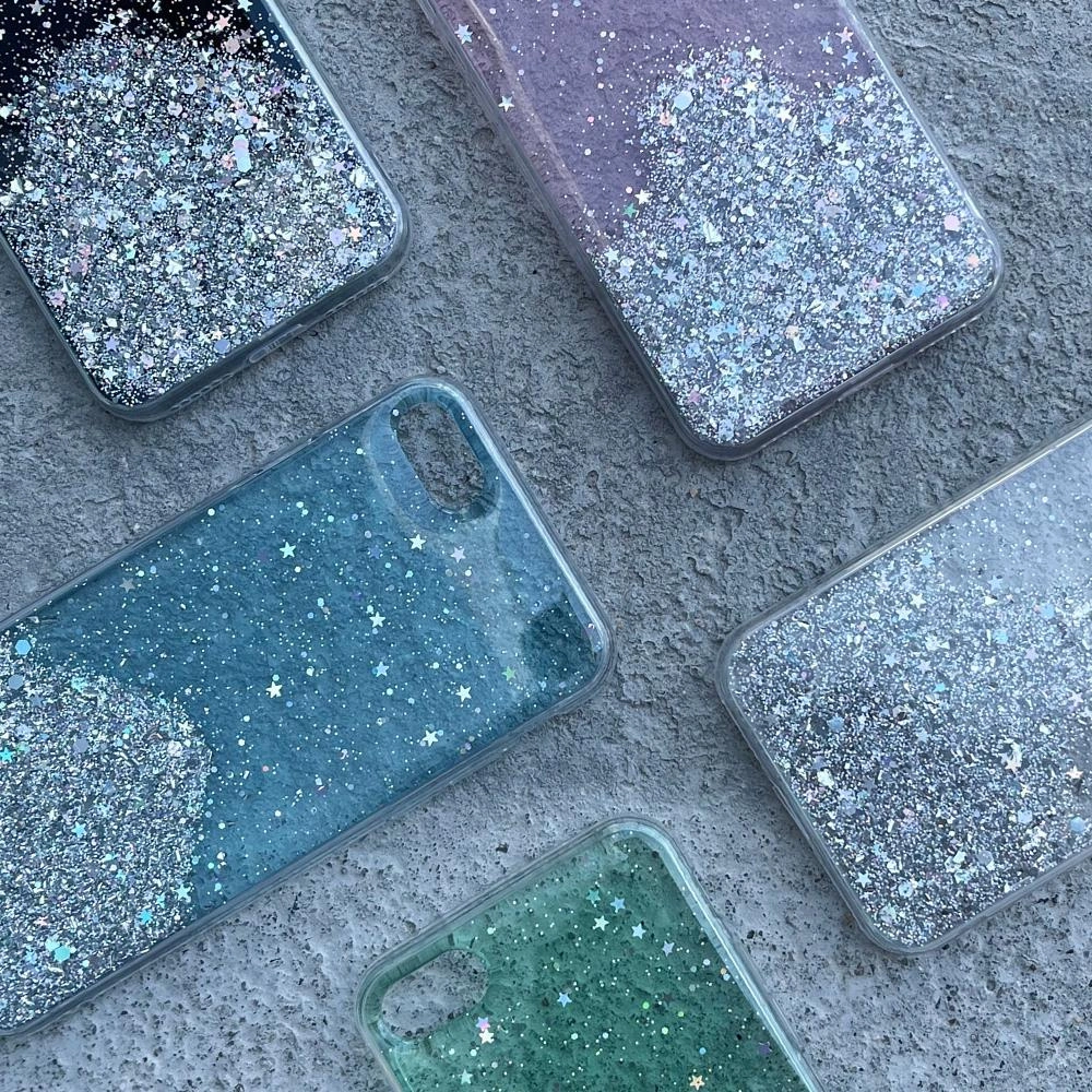 Cinque diverse custodie per cellulari glitterate giacciono su una superficie di cemento grigio.