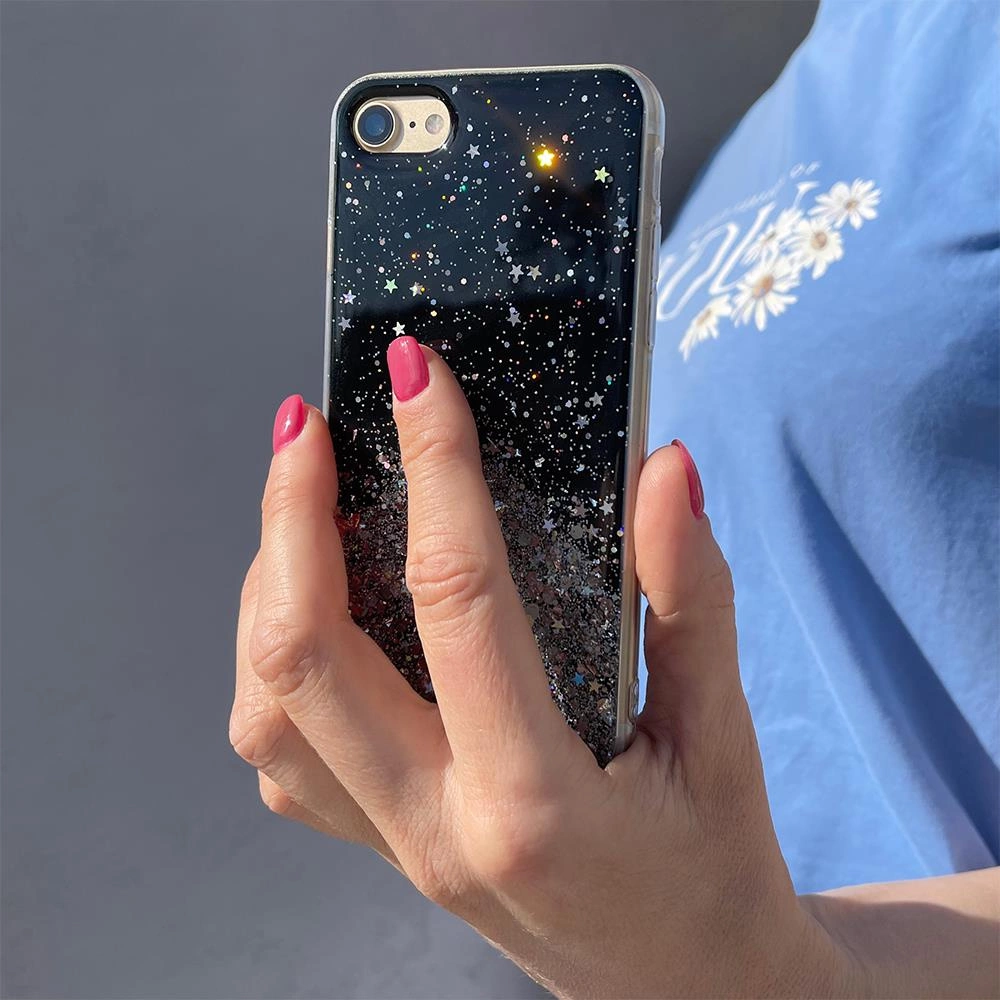 Una mano con unghie rosa regge una custodia per telefono nera, glitterata e stellata.