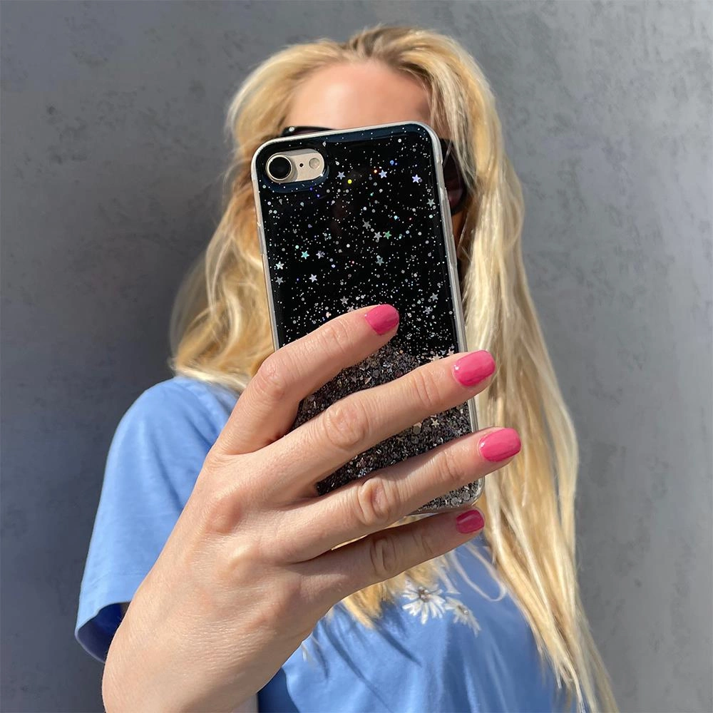 Una donna bionda tiene uno smartphone con una custodia nera glitterata davanti al viso.