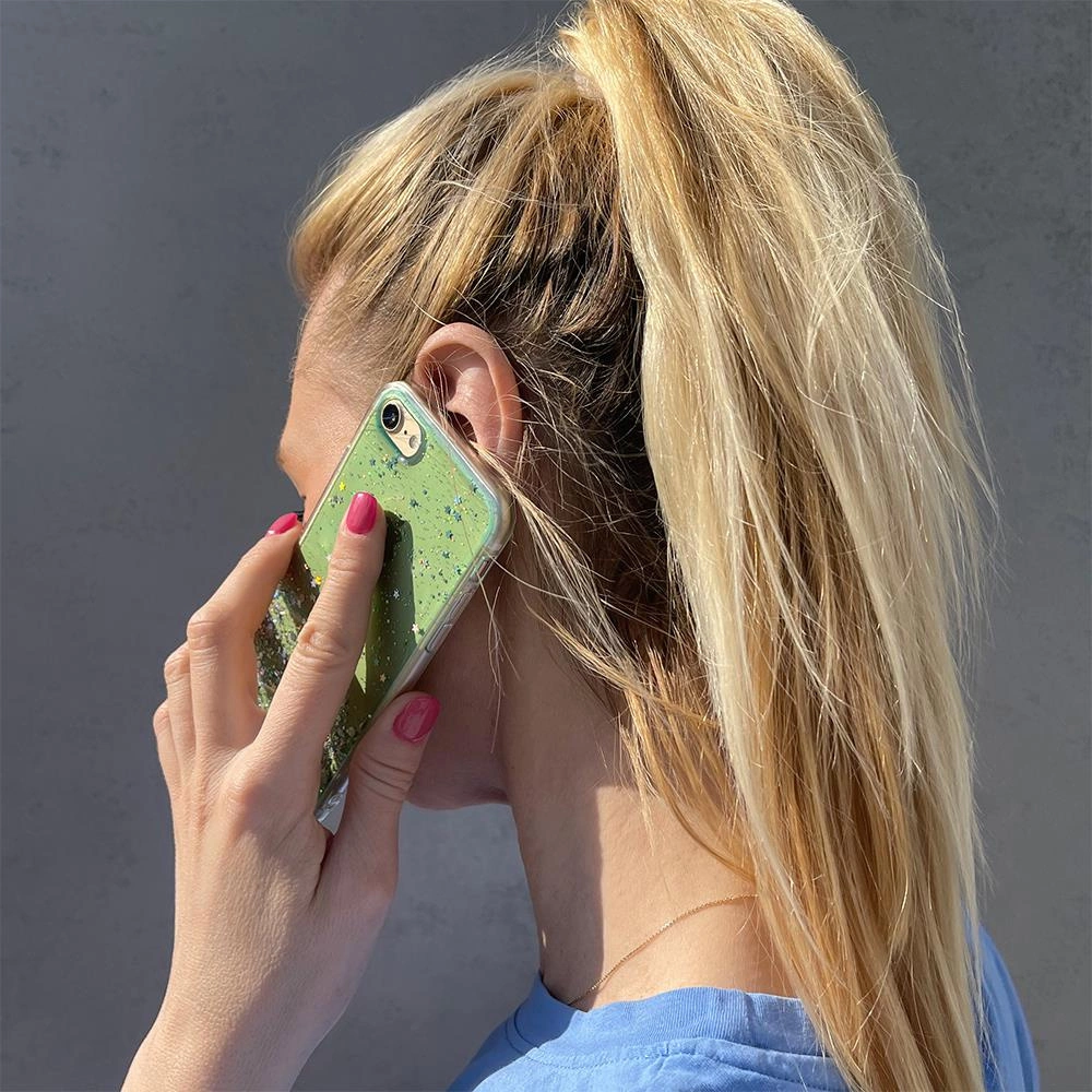 Donna con coda di cavallo bionda telefona con uno smartphone verde glitterato.