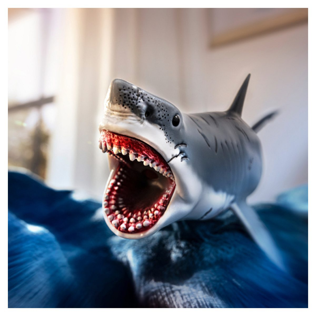 Un petit requin jouet à la bouche ouverte et aux dents visibles nage sur un tissu bleu.