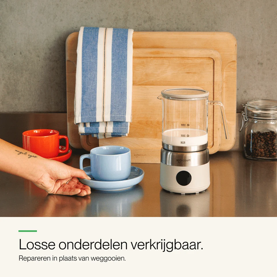 Melkopschuimer, kopjes en kofiebonen op het aanrecht, met houten plank en theedoek op de achtergrond.