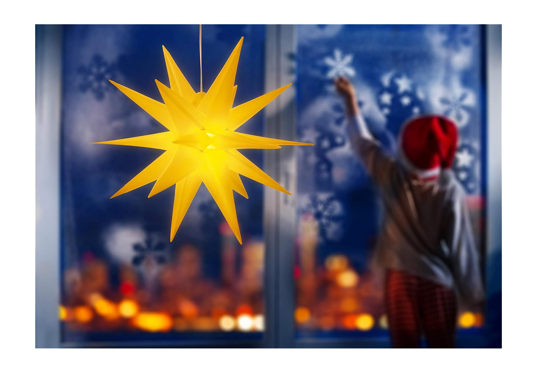 Ein Kind mit Weihnachtsmütze malt Schneeflocken ans Fenster; im Vordergrund hängt ein großer gelber Leuchtstern.