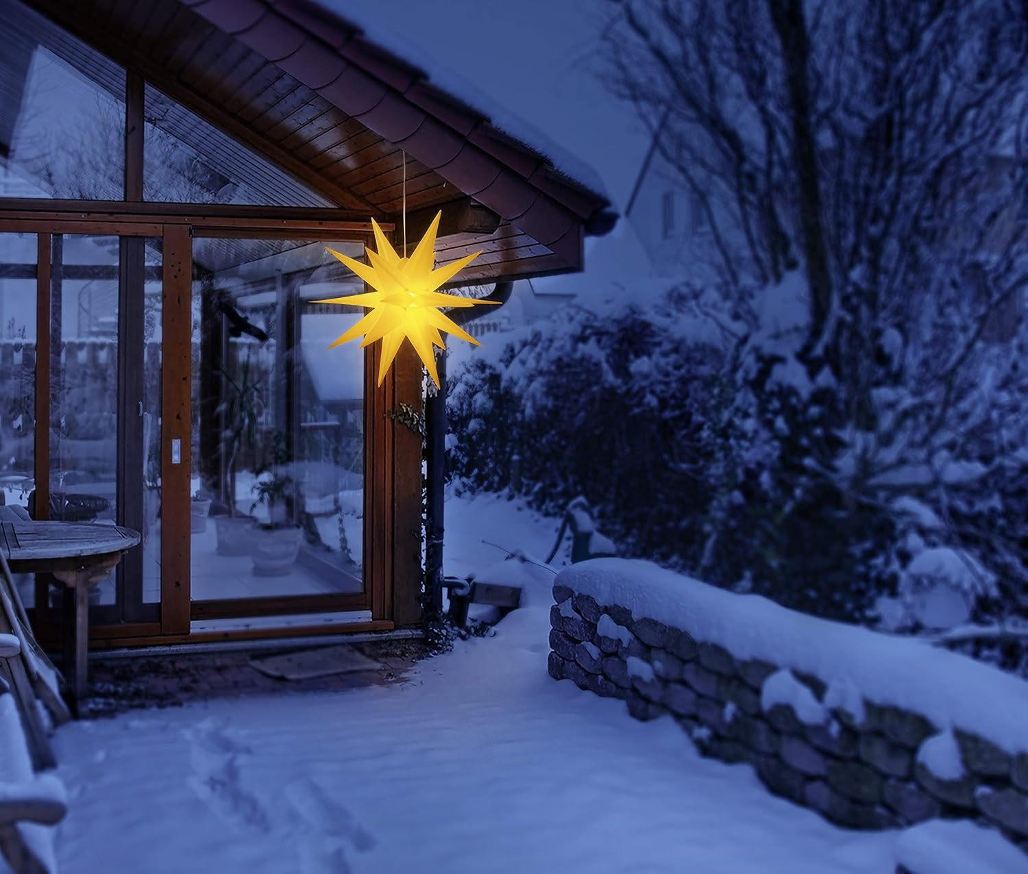 Eine leuchtende gelbe Sternlampe hängt in der Dämmerung auf einer schneebedeckten Terrasse.