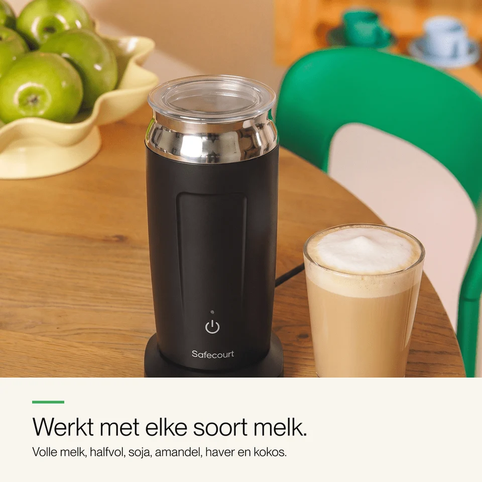 Un mousseur à lait noir et un verre de cappuccino sur une table en bois, avec des pommes vertes en arrière-plan.