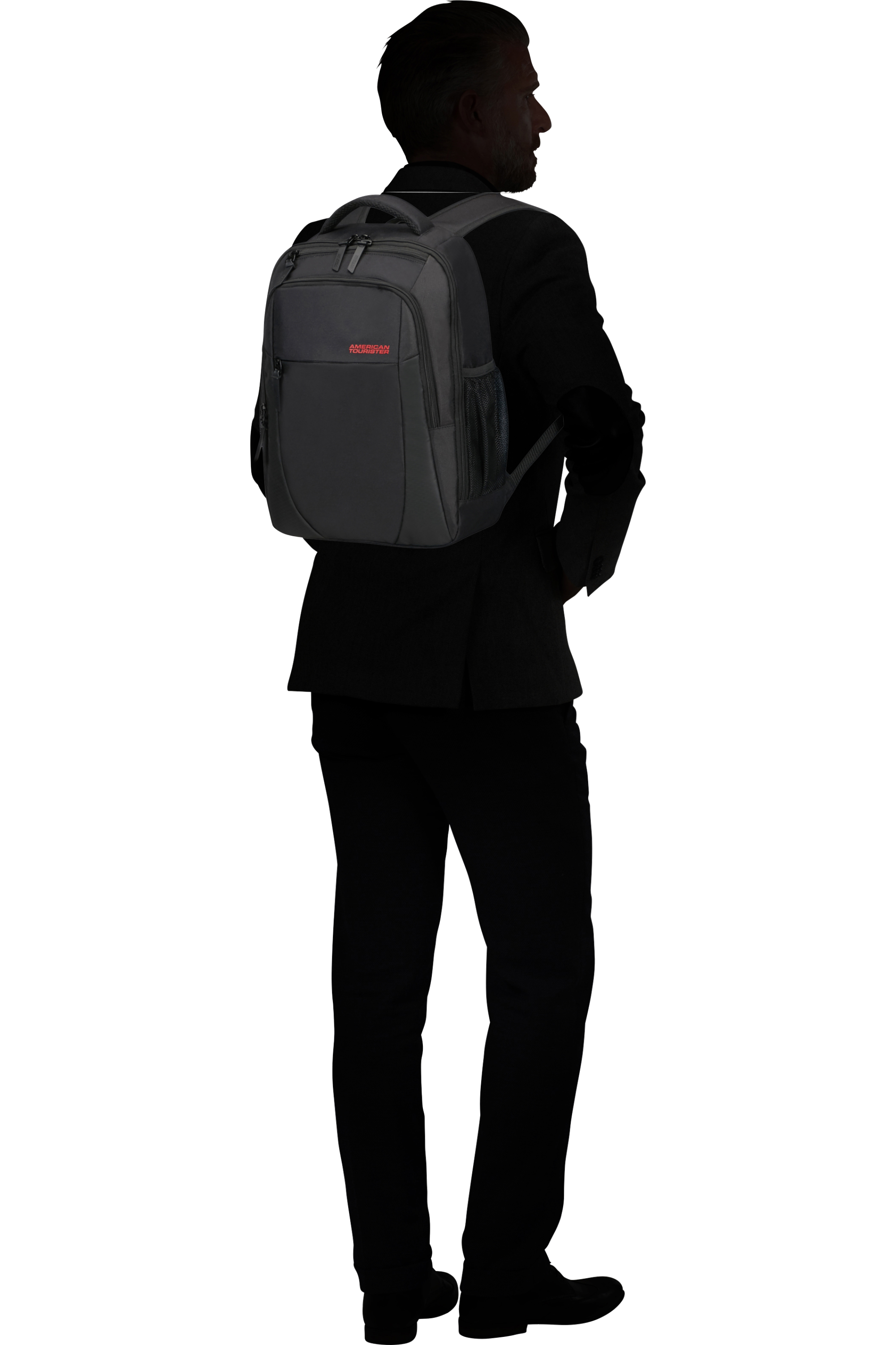 Un uomo in abiti scuri di profilo indossa uno zaino grigio American Tourister sulla schiena.
