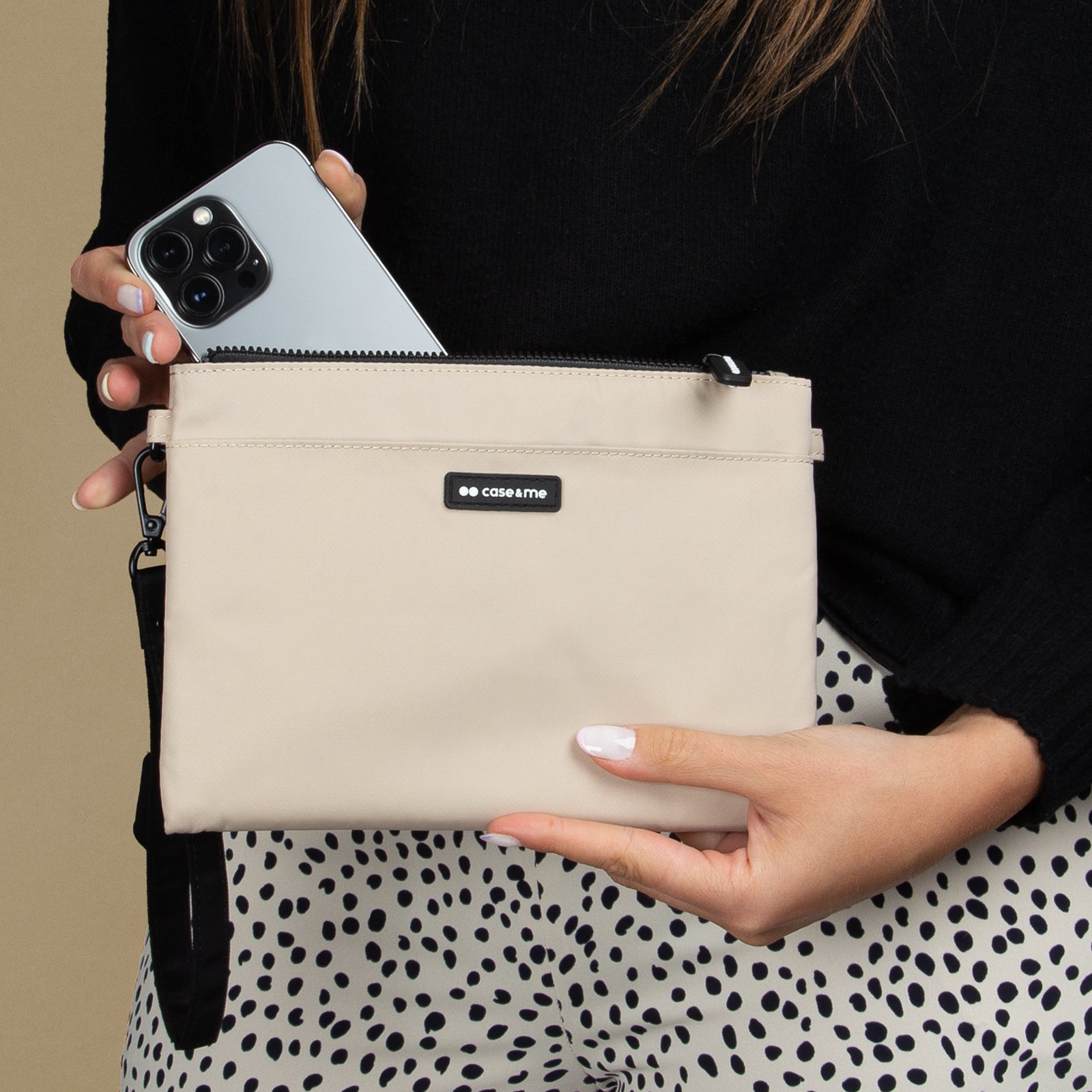 Una mujer con un jersey negro y pantalones de lunares en blanco y negro sostiene una bolsa beis y un teléfono.